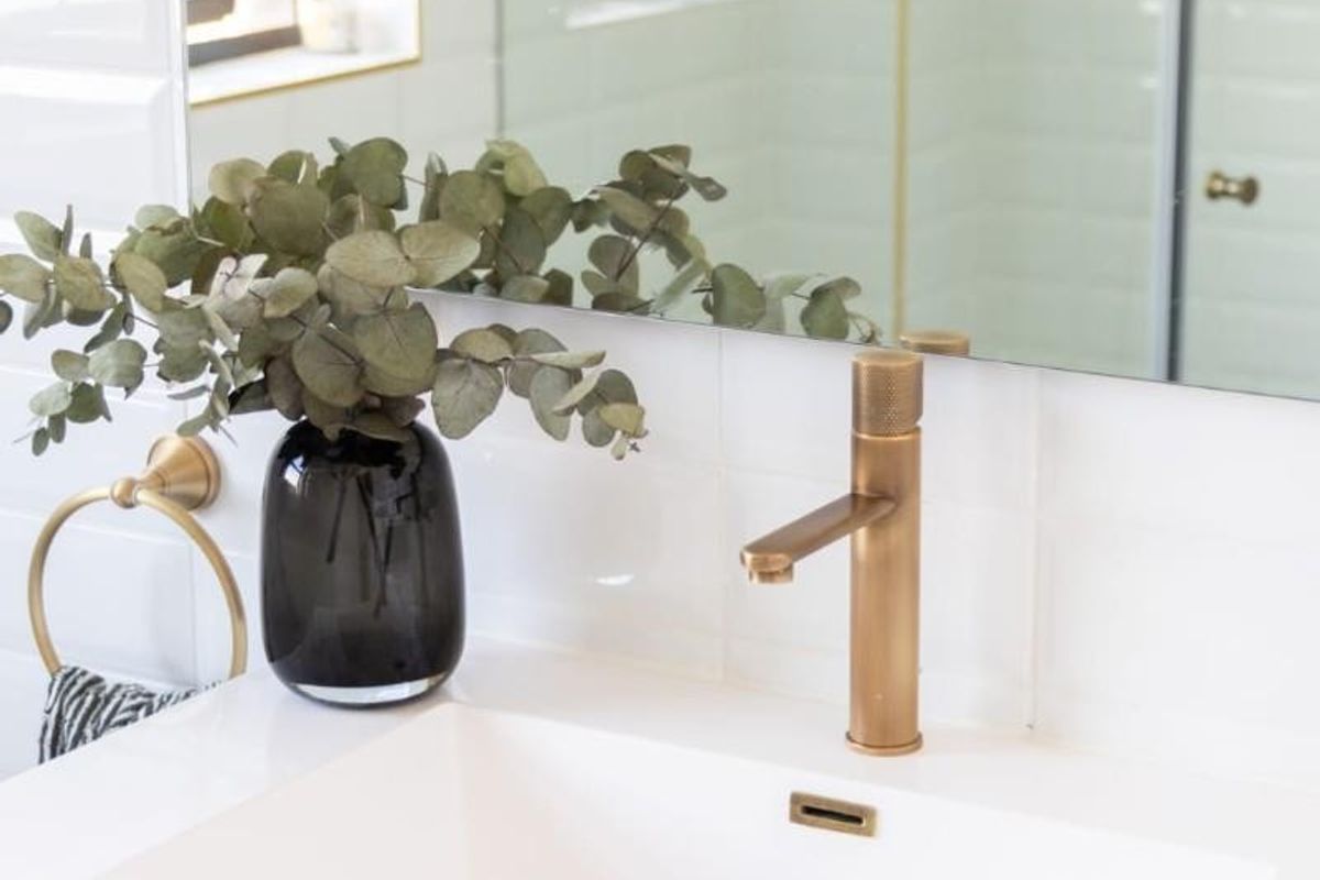 Modern bathroom vanity featuring a white basin, elegant brass faucet, tiled splashback, and a large wall mirror with a glass shower enclosure.