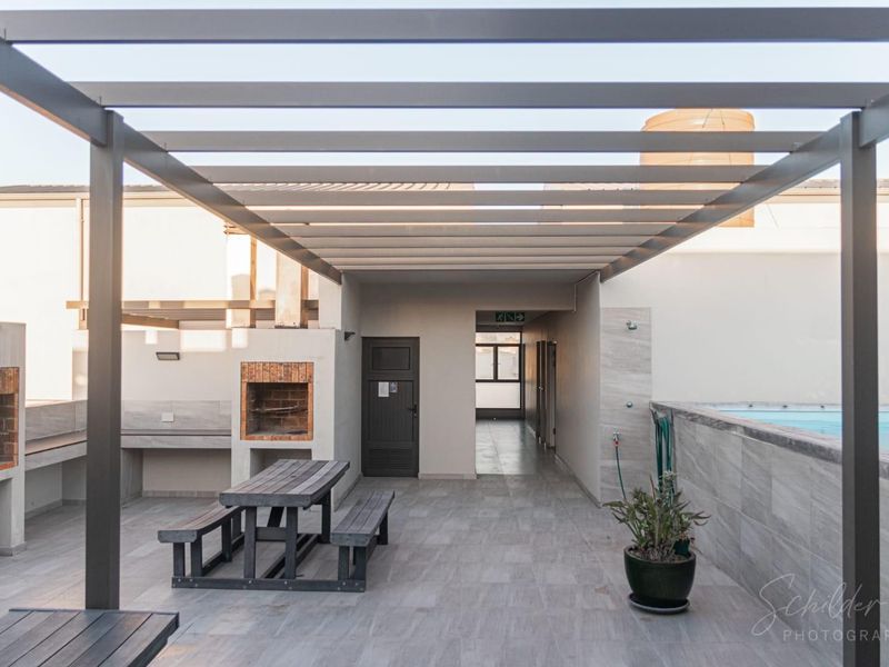 Outdoor entertainment area featuring a swimming pool, built-in braai, and a modern pergola structure with tiled flooring.