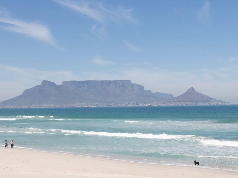 A scenic coastal view featuring the ocean, sandy beach, and Table Mountain in the distance.