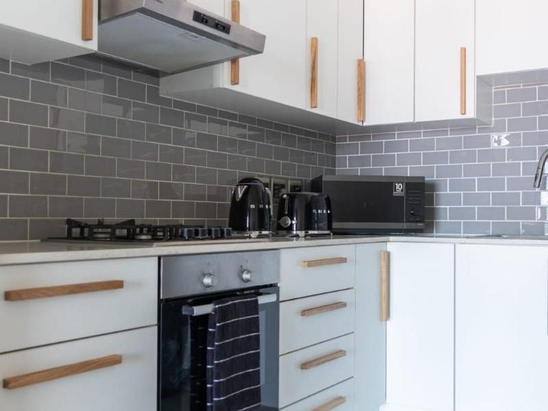 Modern kitchen featuring white cabinetry with timber handles, grey subway tile backsplash, gas hob, built-in oven, and sleek stone countertops.