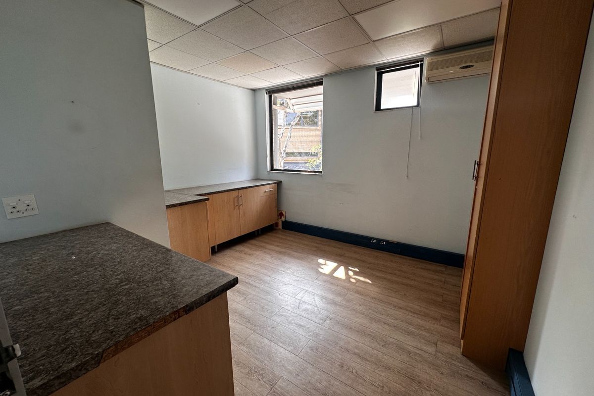 A functional, empty kitchenette area featuring laminate cabinetry, durable countertops, wood-look flooring, and a wall-mounted air conditioning unit.
