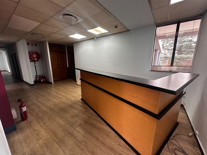 A commercial reception area featuring a built-in reception desk, suspended ceiling with recessed lighting, and wood-look laminate flooring.