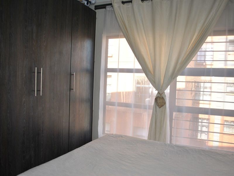 A bedroom featuring dark wood-finish built-in wardrobes and a window with security bars, providing natural light.