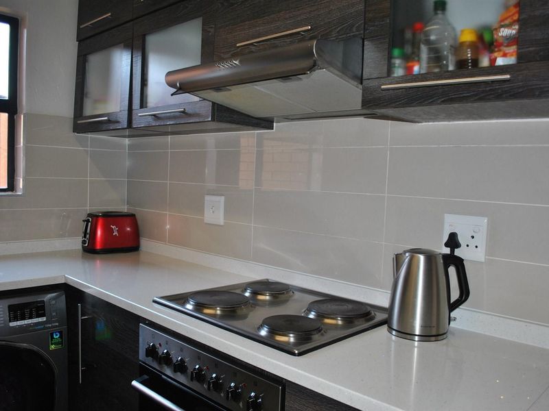 Modern kitchen featuring dark wood cabinetry, stone countertops, tiled splashback, and integrated electric hob with extractor fan.