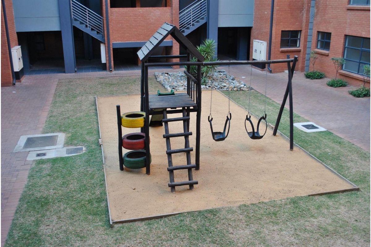 An elevated view of a communal courtyard area featuring a brick building facade, paved walkways, and a central children's play structure.
