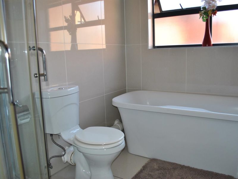 A modern bathroom featuring a freestanding bathtub, a separate shower enclosure, and neutral wall tiling, complemented by a top-hung window for natural light.