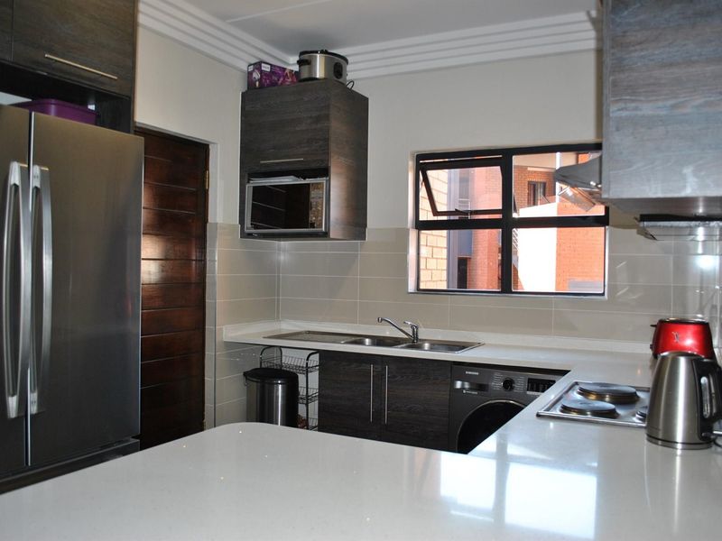 Modern kitchen featuring dark wood cabinetry, stone countertops, integrated microwave, electric hob, and tiled splashback with a functional layout.