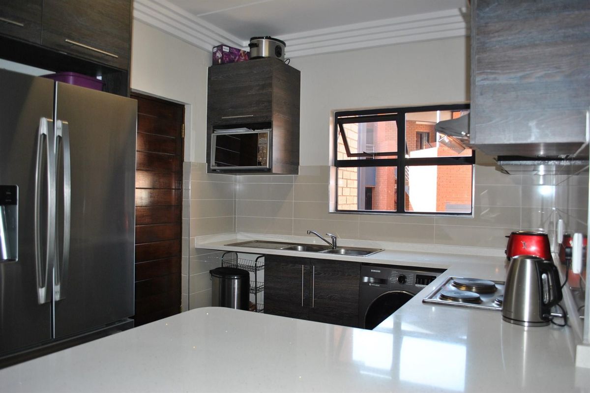 Modern kitchen featuring dark wood cabinetry, stone countertops, integrated microwave, electric hob, and tiled splashback with a functional layout.