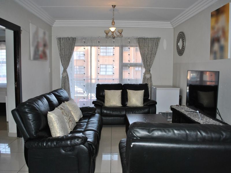 A well-lit living room featuring tiled flooring, decorative ceiling cornices, and a sliding glass door providing access to an outdoor balcony area.