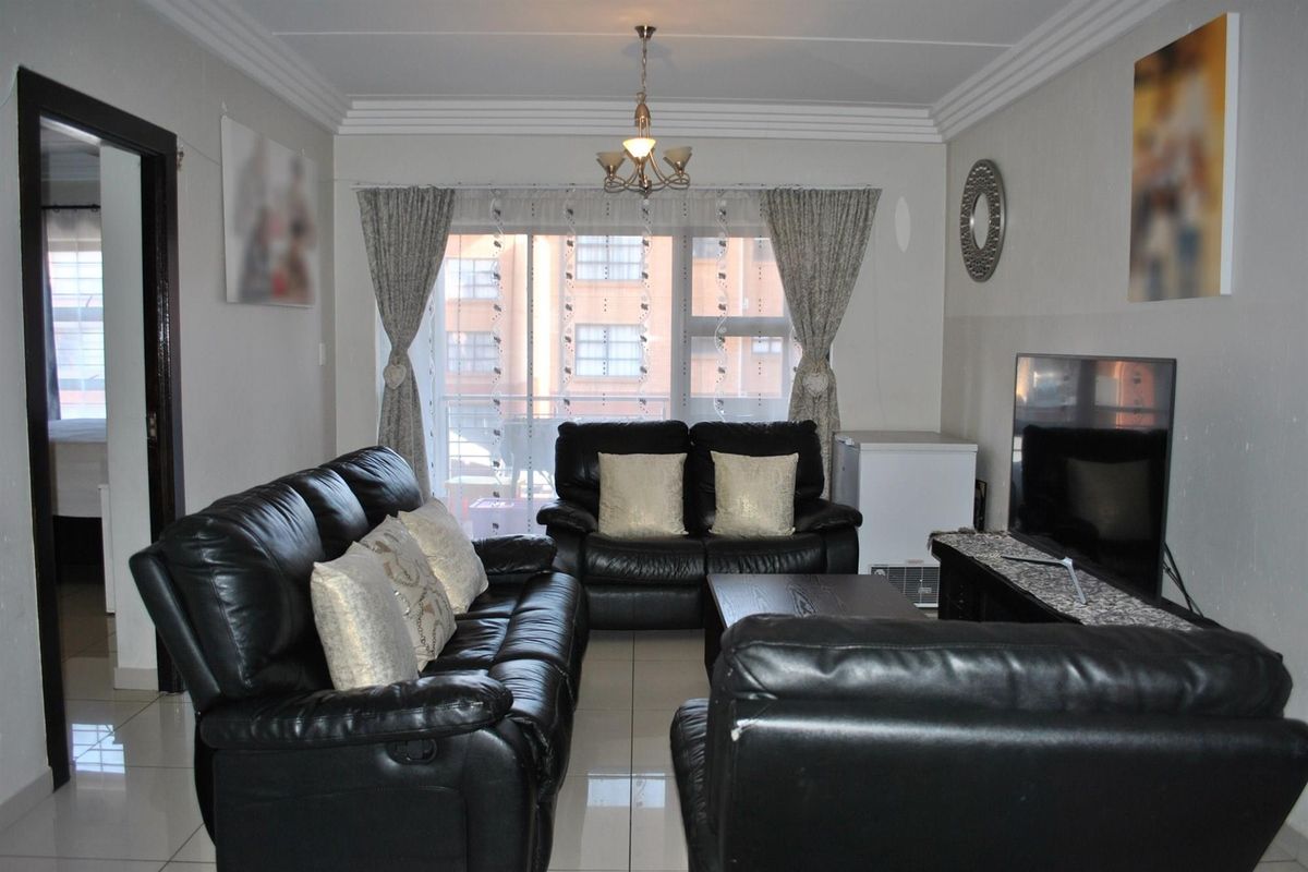 A well-lit living room featuring tiled flooring, decorative ceiling cornices, and a sliding glass door providing access to an outdoor balcony area.