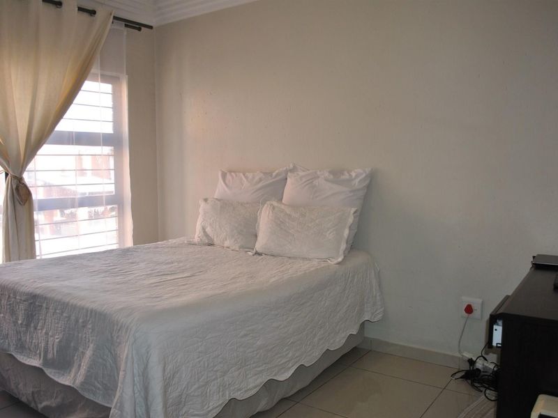 A functional bedroom featuring tiled flooring, neutral walls, and a louvered window allowing natural light into the space.