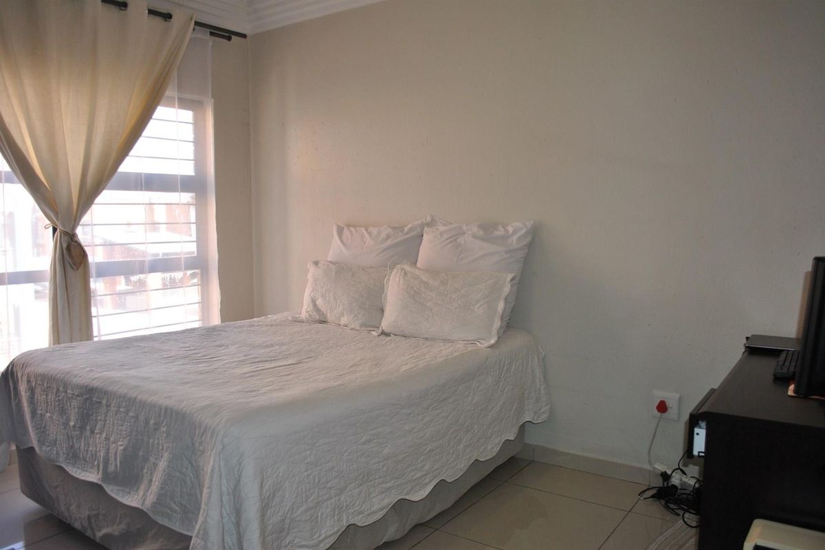 A functional bedroom featuring tiled flooring, neutral walls, and a louvered window allowing natural light into the space.