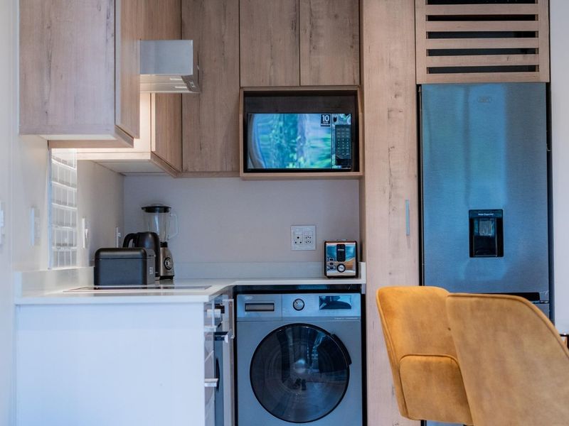 Modern kitchen featuring light wood cabinetry, stone countertops, tiled backsplash, and integrated appliances including a washing machine and microwave.