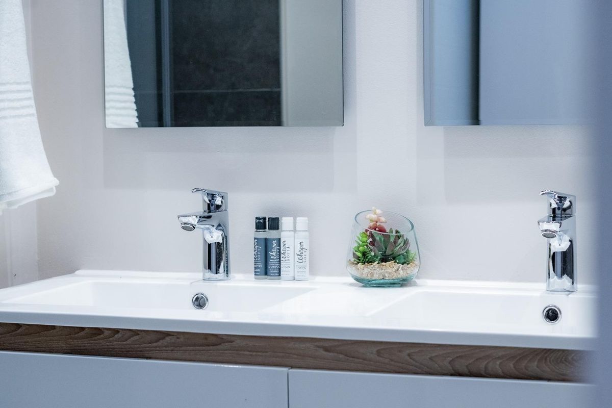 A modern bathroom vanity featuring a double basin, chrome mixer taps, and wall-mounted mirrors with clean, contemporary cabinetry.