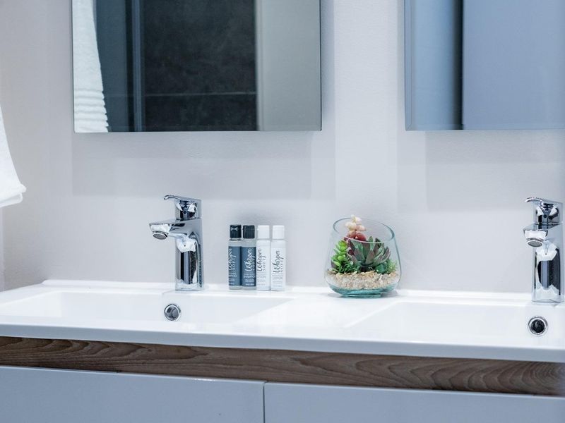 A modern bathroom vanity featuring a double basin, chrome mixer taps, and wall-mounted mirrors with clean, contemporary cabinetry.