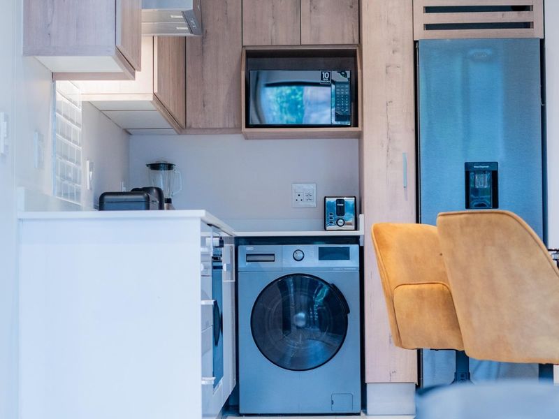 Modern kitchen featuring light wood-tone cabinetry, stone countertops, a tiled backsplash, and integrated appliances including a built-in microwave and washing machine.