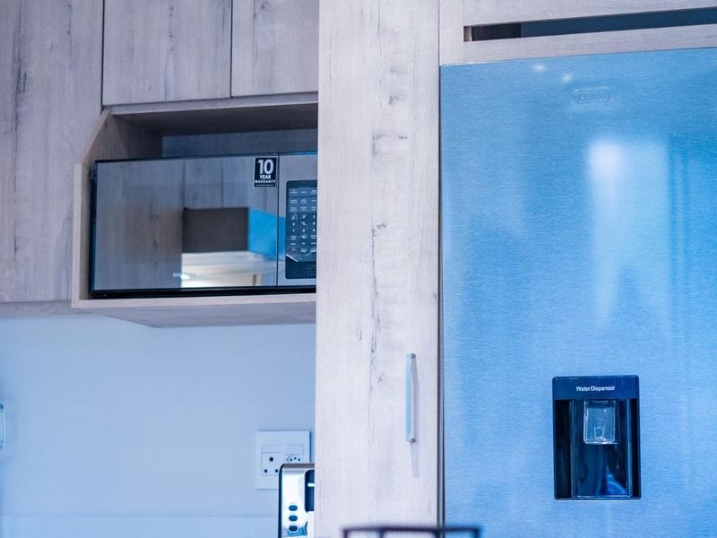 Modern kitchen featuring light wood-grain cabinetry, a built-in microwave, and a stainless steel refrigerator with a water dispenser.