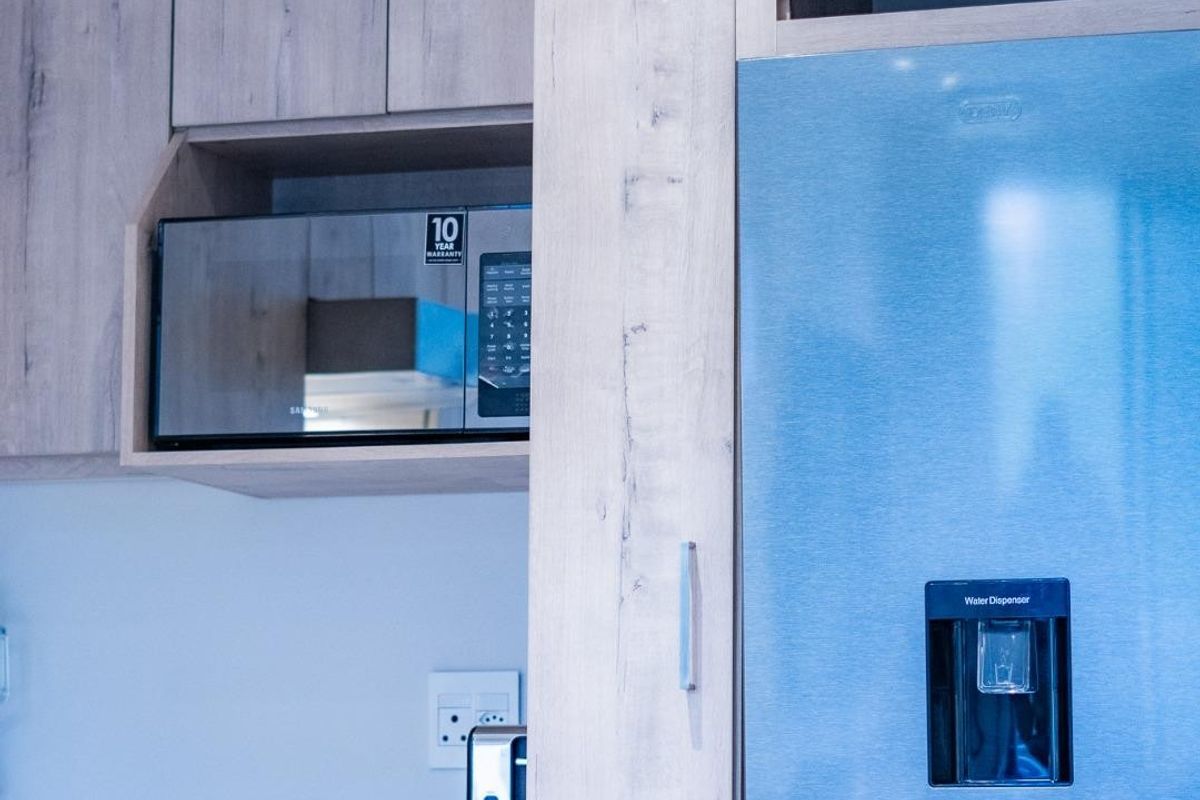 Modern kitchen featuring light wood-grain cabinetry, a built-in microwave, and a stainless steel refrigerator with a water dispenser.