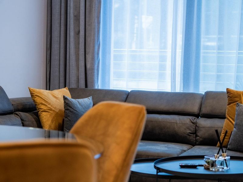 A well-lit living area featuring large windows with floor-to-ceiling curtains, providing a bright and comfortable atmosphere.