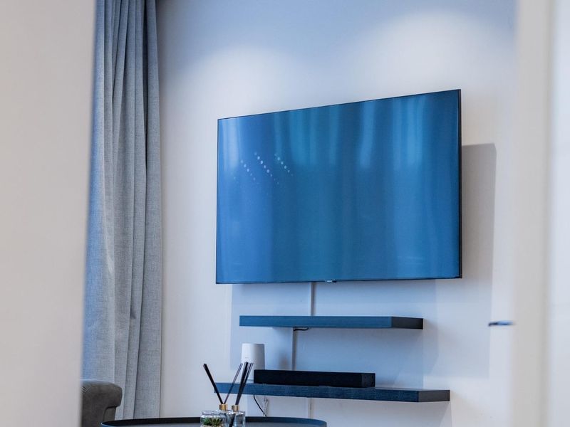 A modern living room wall featuring a mounted television and minimalist floating shelves with integrated curtain treatments.