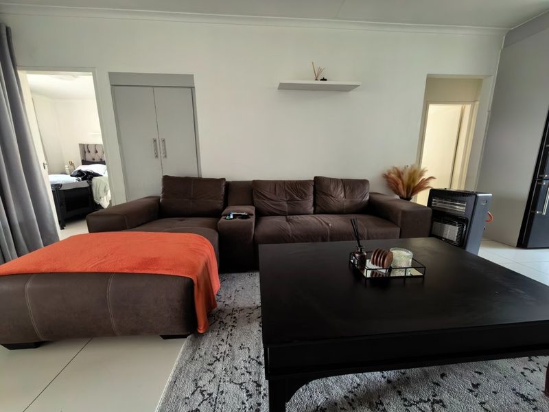 A well-maintained living room featuring neutral tiled flooring, a built-in storage cupboard, and a floating wall shelf, providing a clean and functional living space.