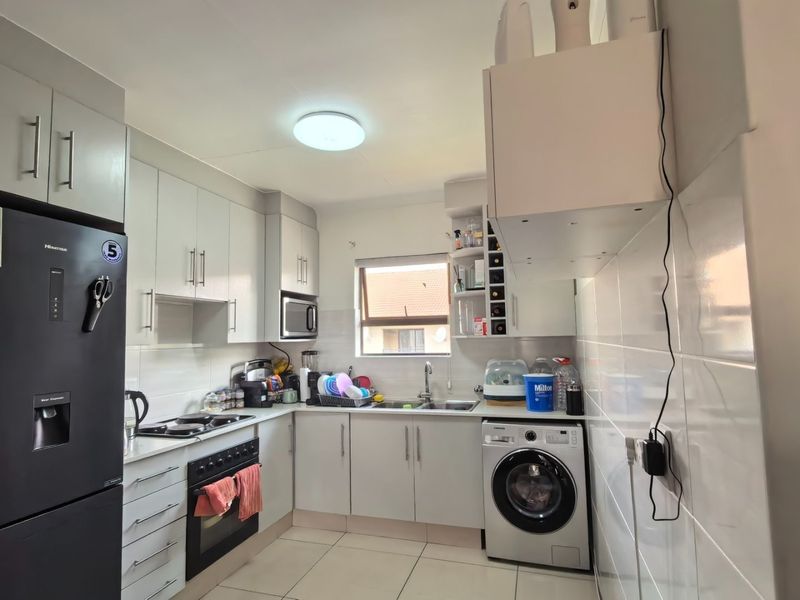 A functional kitchen featuring white cabinetry, tiled splashbacks, built-in oven and hob, and integrated space for a washing machine.