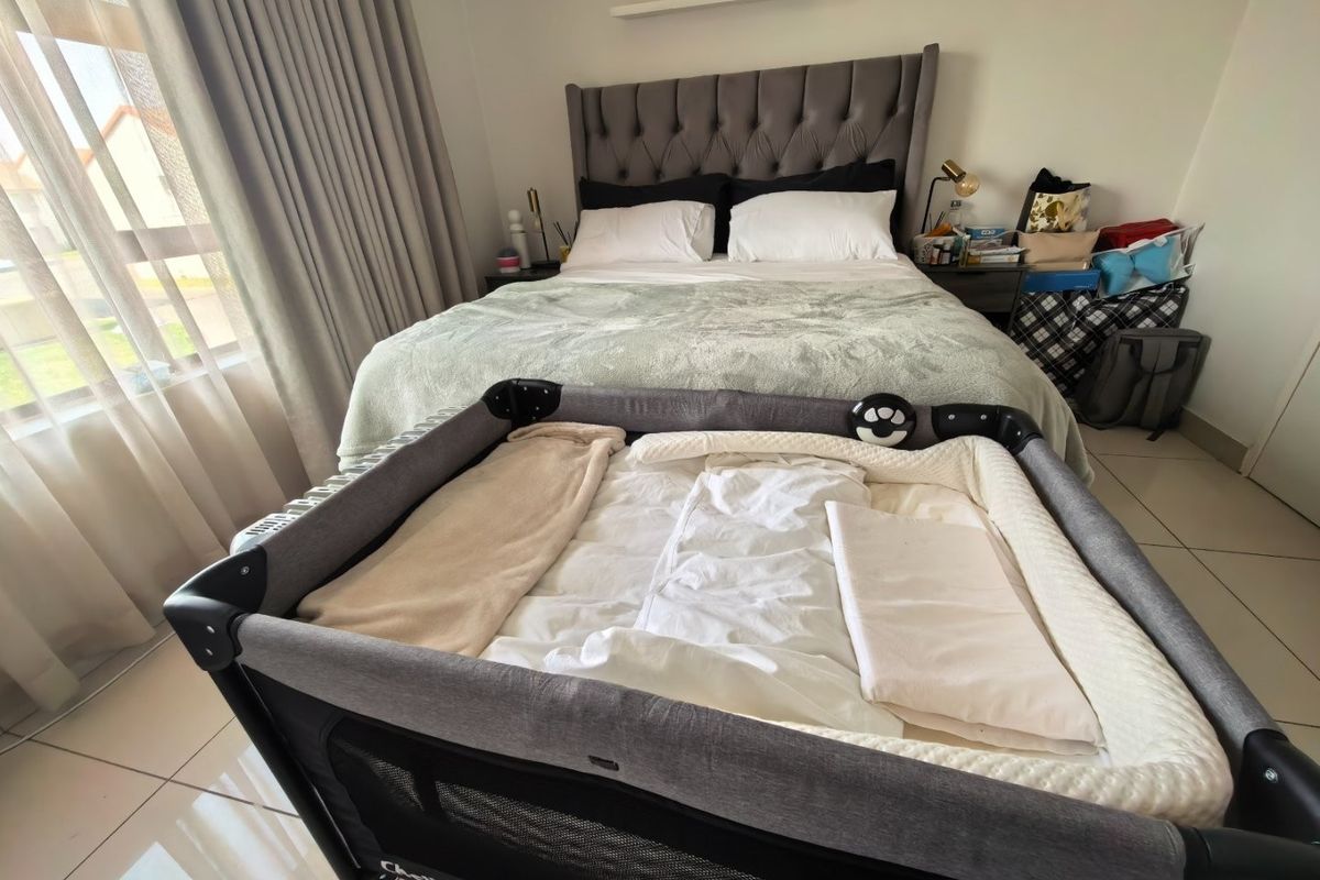 A well-lit bedroom featuring neutral tiled flooring and large windows with curtain tracks, providing a comfortable and functional living space.