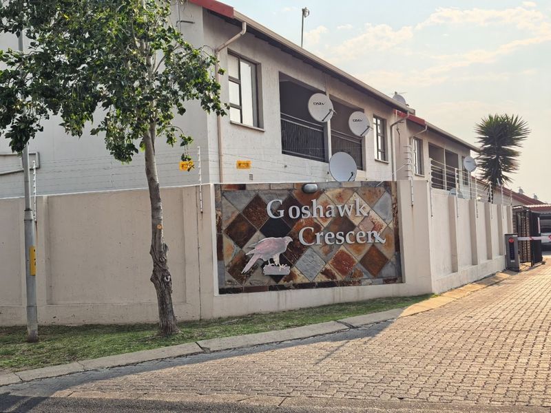 Exterior view of the Goshawk Crescent apartment complex, featuring a paved entrance, perimeter wall with electric fencing, and building facade.