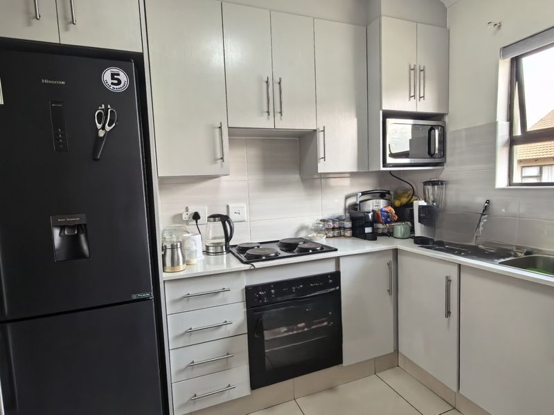 A functional kitchen featuring white cabinetry, a built-in oven and hob, integrated microwave, tiled backsplash, and a stainless steel sink.