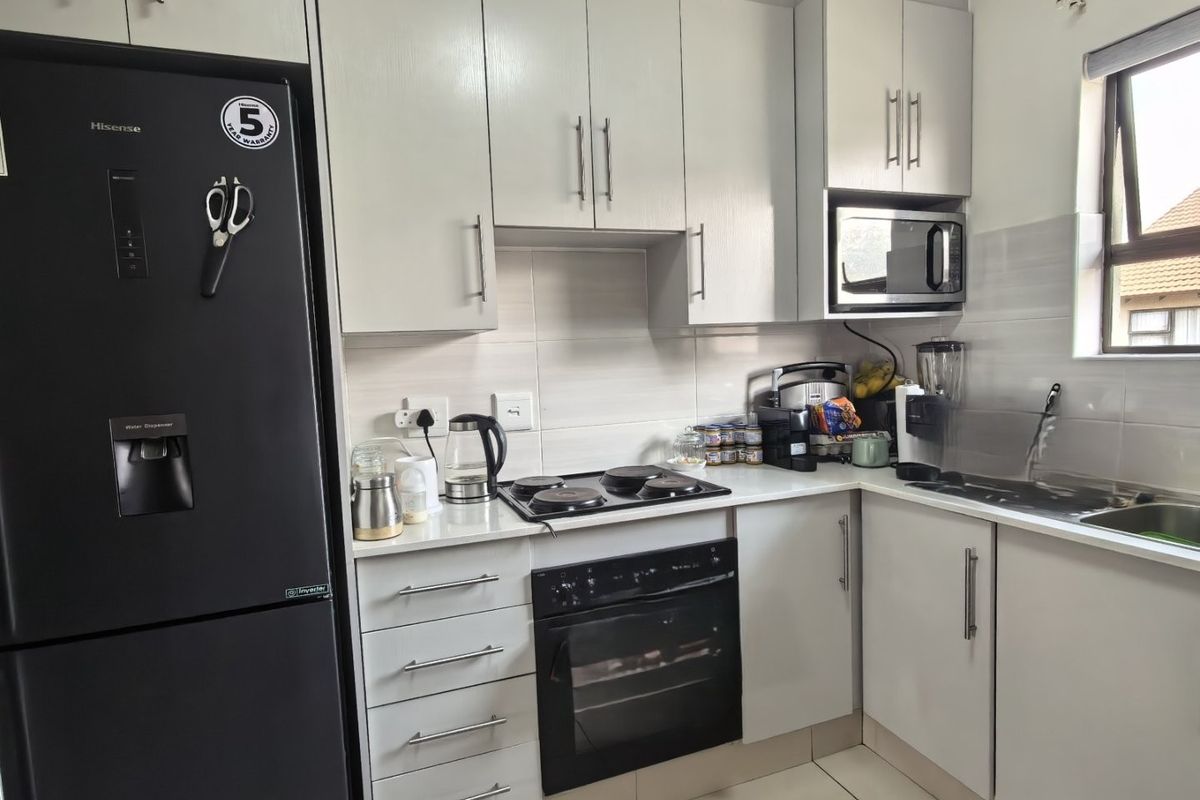 A functional kitchen featuring white cabinetry, a built-in oven and hob, integrated microwave, tiled backsplash, and a stainless steel sink.