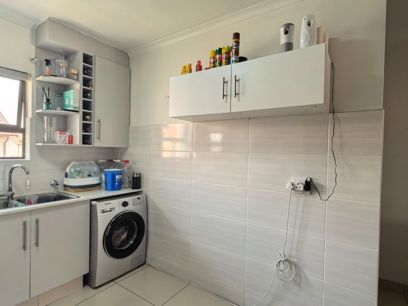 A functional laundry area featuring built-in white cabinetry, a stainless steel sink, tiled splashbacks, and dedicated space for a washing machine.