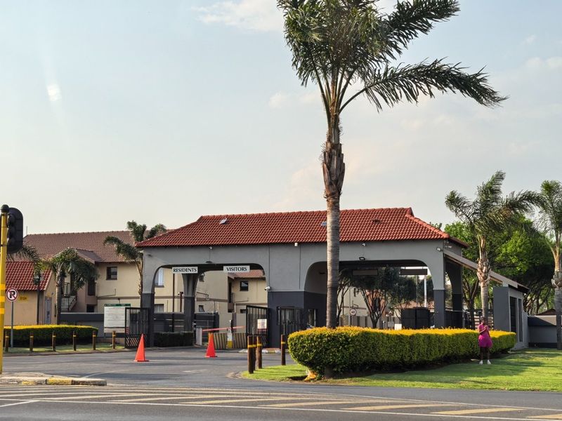 The main entrance and security gatehouse of the apartment complex, featuring dedicated lanes for residents and visitors with controlled access.