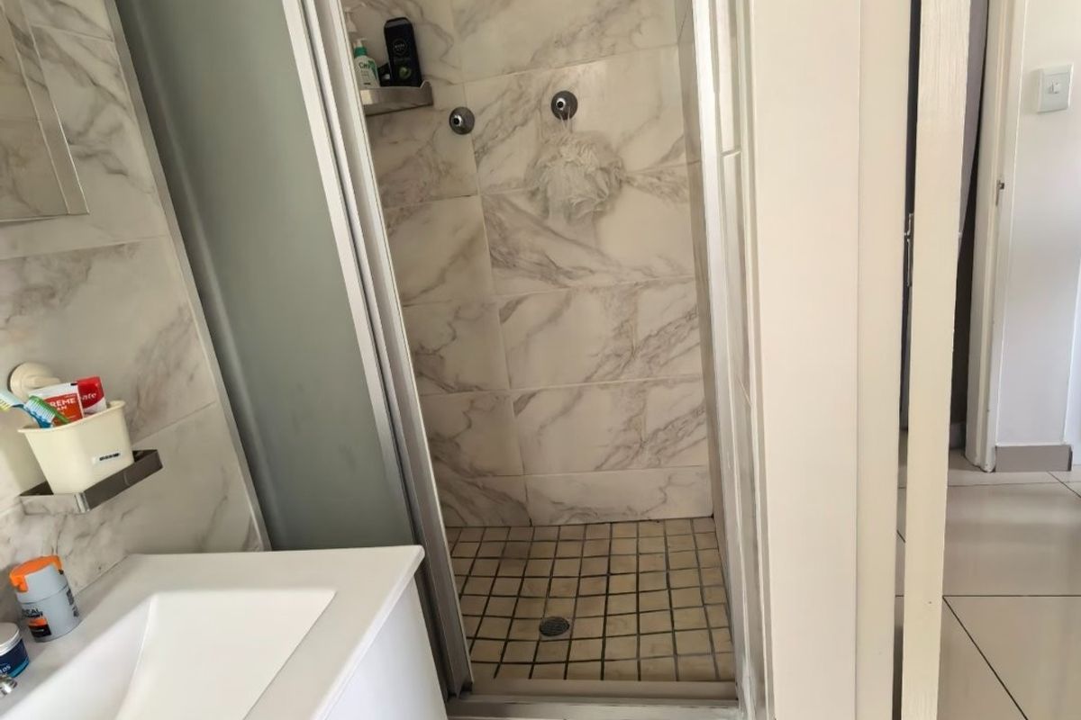 A compact bathroom featuring a modern vanity with integrated basin and a separate shower enclosure with marble-look wall tiling.