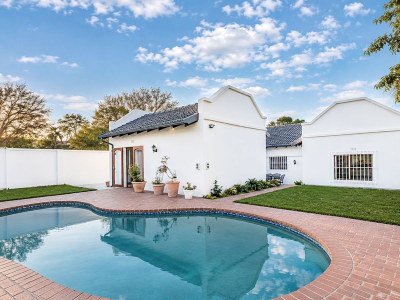 A well-maintained rear garden area featuring a swimming pool with brick coping, surrounded by manicured lawn and white exterior building facades.