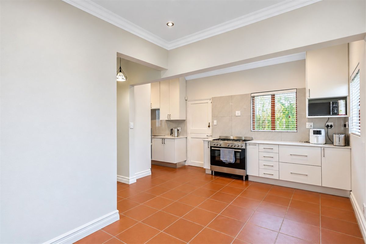 A clean, functional kitchen featuring tiled flooring, ample built-in cabinetry, and a gas stove, with a connected scullery area visible in the background.