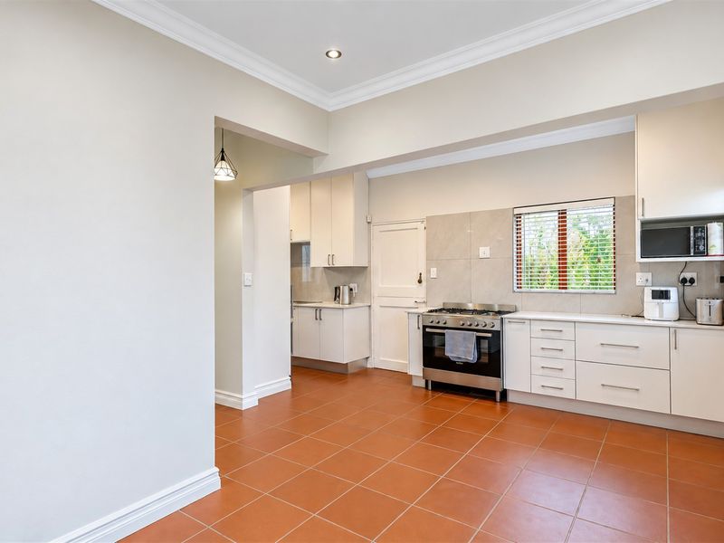A clean, functional kitchen featuring tiled flooring, ample built-in cabinetry, and a gas stove, with a connected scullery area visible in the background.