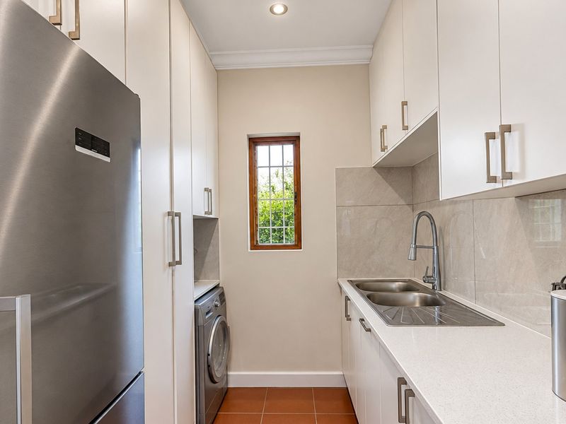 A well-appointed scullery featuring modern white cabinetry, stone benchtops, a double bowl sink, and dedicated space for laundry appliances.