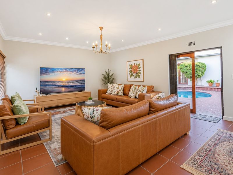 A bright and spacious living room featuring terracotta floor tiles, recessed lighting, and direct access to an outdoor patio and pool area.