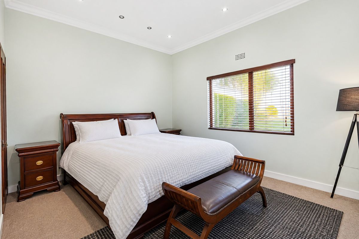 A well-maintained bedroom featuring neutral wall tones, carpeted flooring, recessed downlights, and a window with timber venetian blinds.