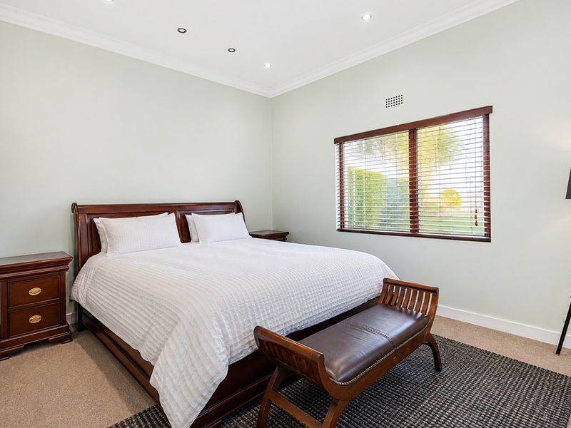 A well-maintained bedroom featuring neutral wall tones, carpeted flooring, recessed downlights, and a window with timber venetian blinds.