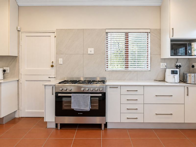 A well-maintained kitchen featuring white cabinetry, stone countertops, a gas stove with electric oven, and neutral tiled flooring.