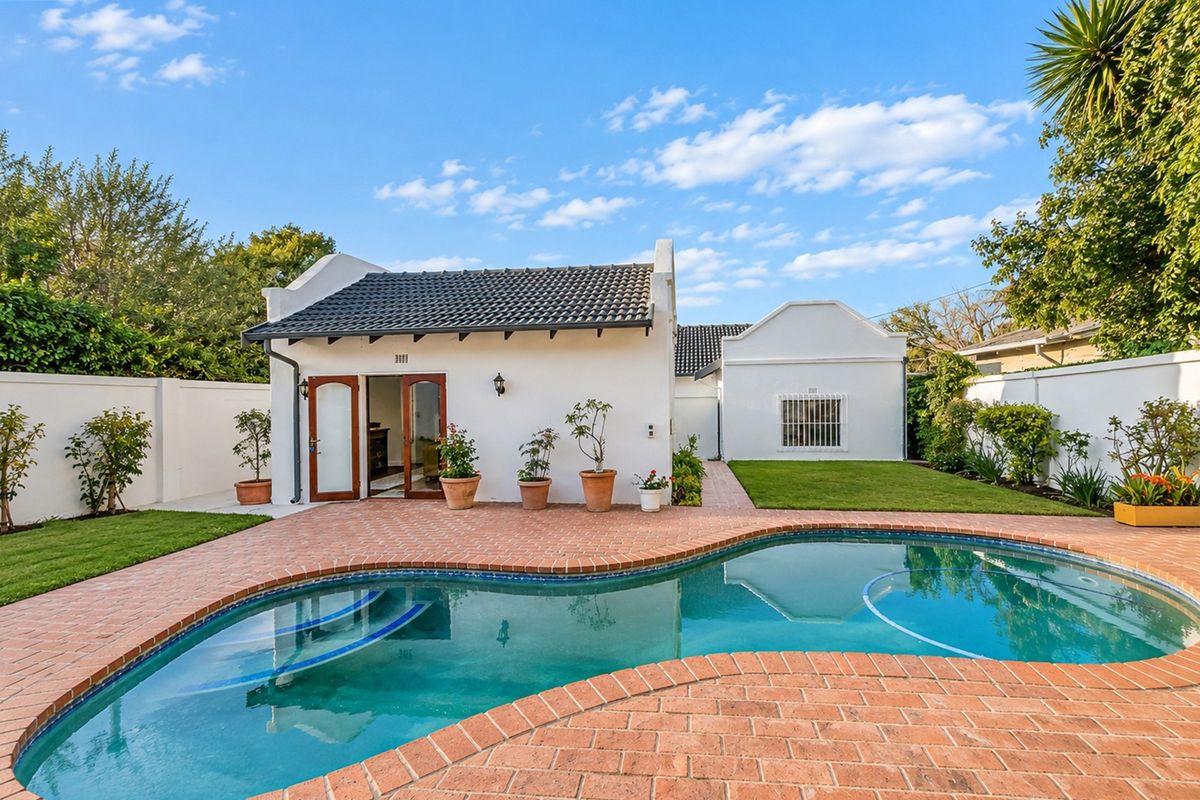 A well-maintained rear exterior view featuring a swimming pool, brick-paved patio area, and a white-walled structure with a tiled roof.