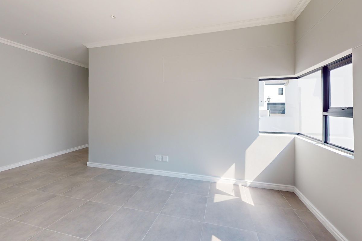 A bright, empty bedroom featuring neutral tiled flooring, clean walls, and a modern corner window allowing for ample natural light.