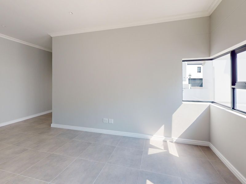 A bright, empty bedroom featuring neutral tiled flooring, clean walls, and a modern corner window allowing for ample natural light.
