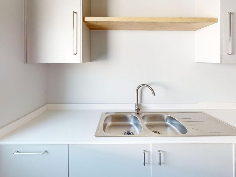 A clean, modern kitchen area featuring a stainless steel double sink, neutral cabinetry, and a floating timber shelf.