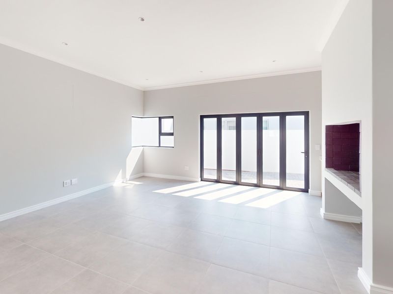 Spacious, light-filled living area featuring neutral tiled flooring, a built-in fireplace, and modern aluminium stacker doors opening to the exterior.