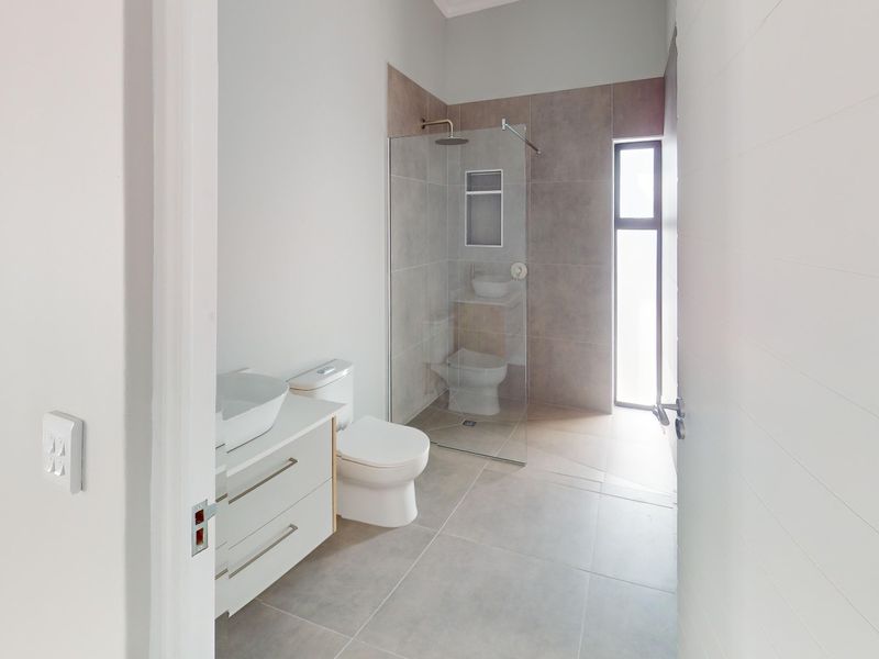 Modern bathroom featuring a glass-enclosed shower, contemporary vanity with vessel sink, neutral floor tiles, and clean, minimalist finishes.