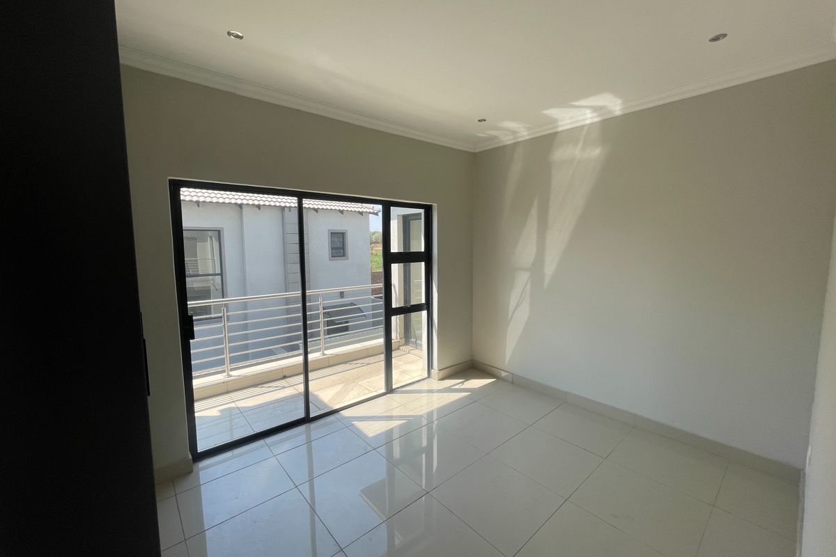 A bright, empty bedroom featuring polished tile flooring, recessed lighting, and a sliding glass door providing direct access to an outdoor balcony.