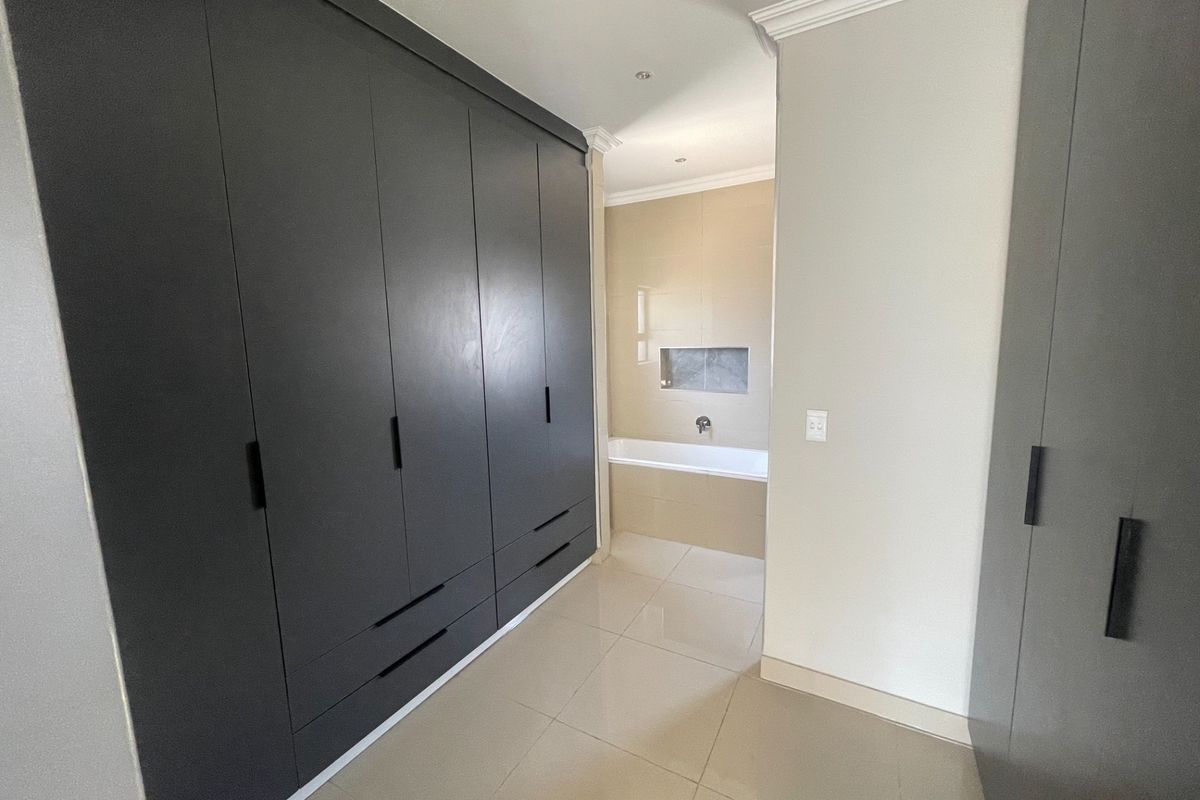 A modern dressing area featuring extensive built-in dark cabinetry leading into a clean, tiled bathroom with a built-in bathtub and recessed wall niche.