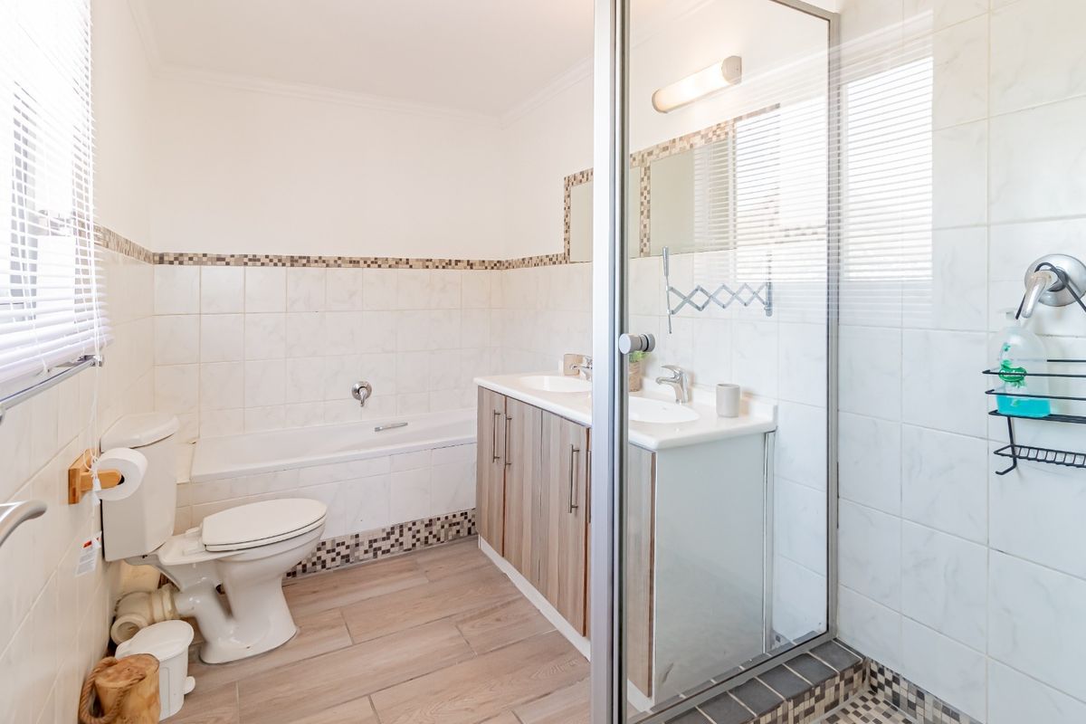 A well-maintained bathroom featuring a built-in vanity, a separate bathtub, and a glass-enclosed shower with neutral tiled finishes.